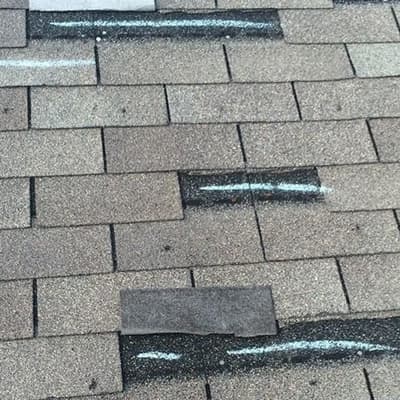 This picture shows black bruises on the three tab shingles. That is hail damage. It also shows shingles torn up from wind damage. This roof needs a repair or to be replaced.